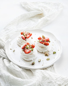 Small strawberry and pistachio pavlova meringue cakes with mascarpone cream  fresh mint over white backdrop