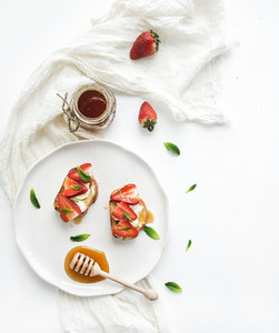 French toasts with strawberry  cream cheese  honey and mint on light ceramic plate over white backdrop