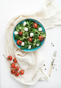 Spring salad with lambs lettuce mozarella and cherry tomatoes in blue ceramic bowl over white backdrop