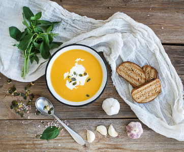 Pumpkin soup with cream  seeds  bread and fresh basil in metal plate on rustic wood background