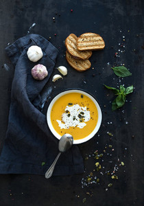 Pumpkin soup with cream  seeds  bread and fresh basil on grunge black background