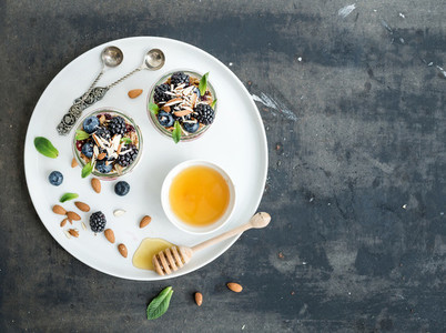 Yogurt oat granola with berries  honey and nuts in glass jars  dark grunge background