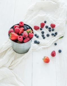 Metal bucket of strawberries  raspberries  blueberries and mint leaves  white wooden background