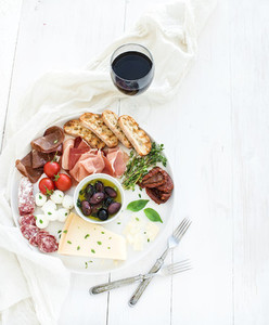 Wine appetizer set  Cherry tomatoes  parmesan cheese  meat variety  bread slices  dried tomatoes  olives and basil on round ceramic plate over white wood backdrop