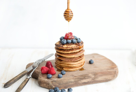 Buckwheat pancakes with fresh berries and honey on rustic wooden board