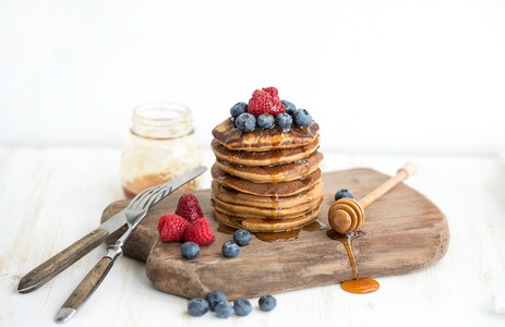 Buckwheat pancakes with fresh berries and honey on rustic wooden board