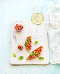 Tomato and basil bruschetta sandwich on white wooden serving board over rustic blue background  top view