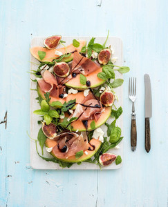 Prosciutto  melon  fig and soft cheese salad on a white serving board over grunge background