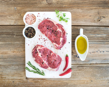 Raw fresh meat Ribeye steak entrecote and seasonings on white cutting board over grunge background