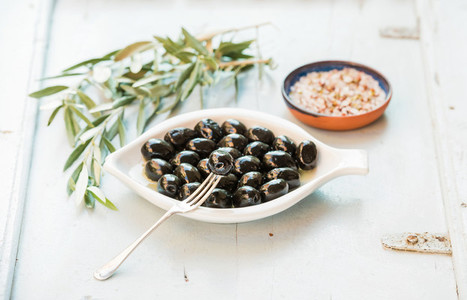 Black olives in white ceramic plate  branches and spices over li