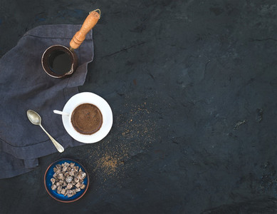 Cup of black coffee with dried figs and cane sugar over dark stone backdrop  top view
