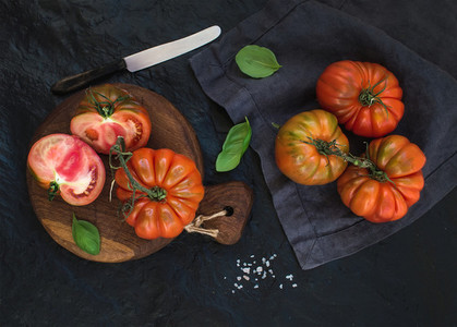 Fresh ripe hairloom tomatoes and basil leaves on rustic wooden board over black stone background  horizontal