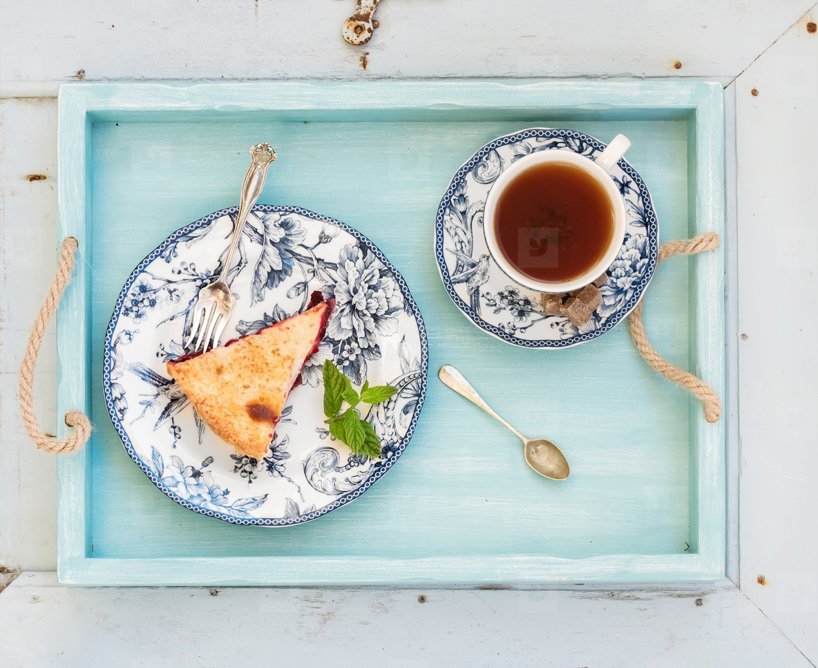 Piece of double crust plum pie and black tea in vintage porcelain cup, blue wooden tray. Top view, horizontal