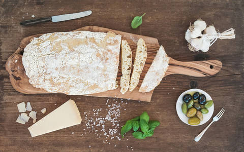 Freshly baked ciabatta bread with garlic mediterranean olives basil and Parmesan cheese on serving board over rustic wooden background