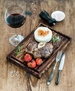 Roast beef Ossobuco with rice  vegetables and glass of wine on serving board over rustic wood background
