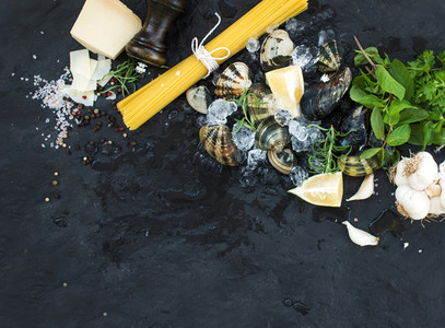 Ingredients for cooking Spaghetti vongole  Clams on chipped ice  raw pasta  Parmesan cheese  garlic  parsley and lemon over stone slate background  top view