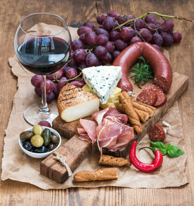 Glass of red wine cheese and meat board grapesfig strawberries honey bread sticks  on rustic wooden table white background