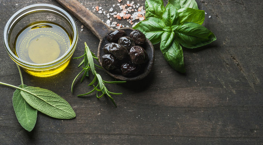 Greek black olives  fresh herbs and oil on dark rustic wooden background
