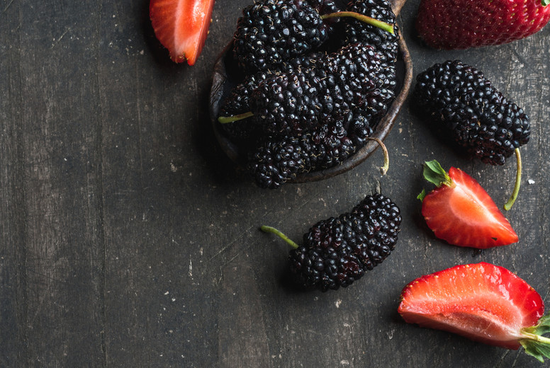 Berries on dark wooden background. Fresh strawberries and mulberries in rustic cooking spoon 