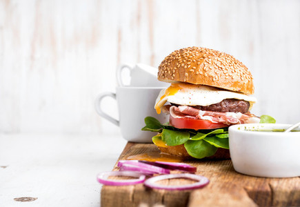 Breakfast set Homemade beef burger with fried egg vegetables onion rings and coffee cups on wooden board