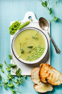 Light summer green pea cream soup in bowl with sprouts  bread toasts and spices