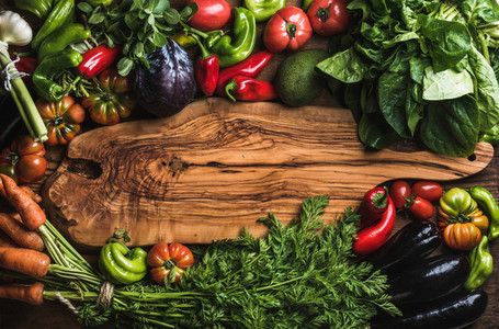 Fresh raw vegetable ingredients for healthy cooking or salad making with rustic olive wood board in center