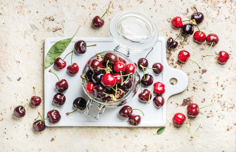 Sweet cherry in glass jar on white board over concrete background