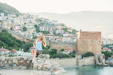 Young blond woman tourist sitting on ancient fortress wall of Alanya castle