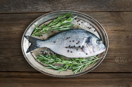 Fresh sea fish dorado on a metal dish with rosemary and spices