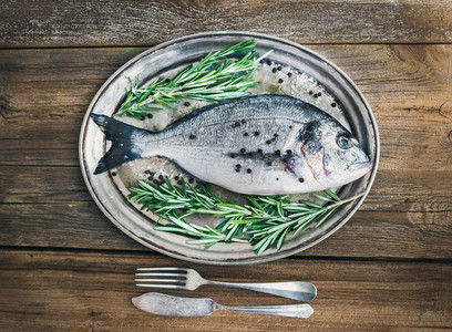 Fresh sea fish sea bream on a metal dish with rosemary and spi