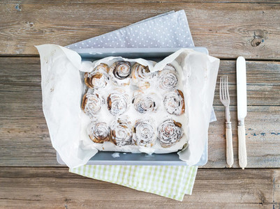Cinnamon buns with cream cheese icing in a baking dish over a ru