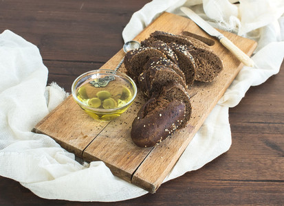 Dark baguette cut in slices with olive oil on a rustic wooden bo