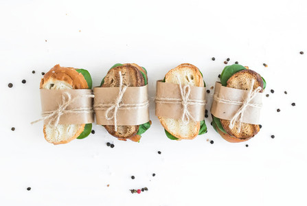 Chicken and spinach sandwiches wrapped in craft paper over a whi