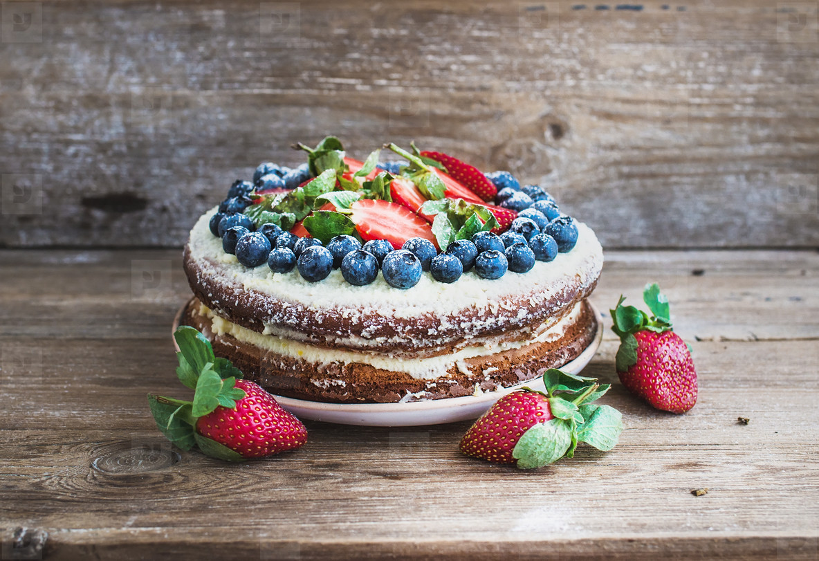 Rustic spicy ginger cake with cream cheese filling  fresh strawberries and blueberries over a rough wood background