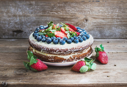 Rustic spicy ginger cake with cream cheese filling fresh strawberries and blueberries over a rough wood background