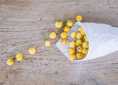 Yellow sweet cherries in a paperbag on a rought wood surface