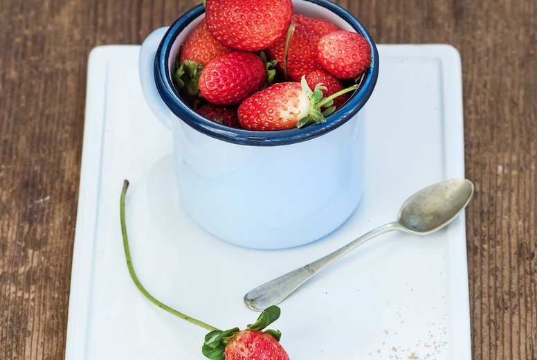Fresh ripe red strawberries in blue enamel mug on white ceramic board over rustic wooden background