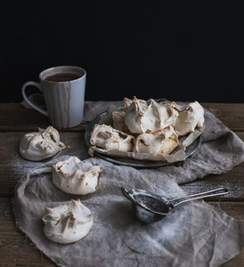 Meringues and mug of hot chocolate on a rustic wooden table  Black background