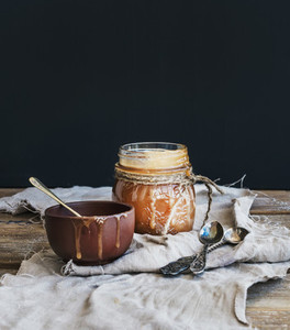 Salted caramel sauce in a rustic glass jar and brown ceramic cup on wooden desk