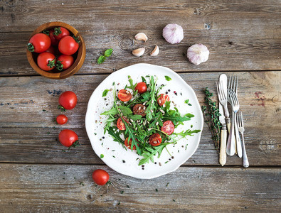 Salad with arugula  cherry tomatoes  sunflower seeds and herbs on white ceramic plate over rustic wood background