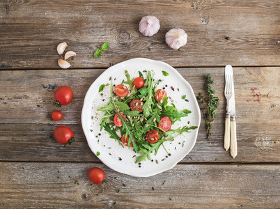 Salad with arugula  cherry tomatoes  sunflower seeds and herbs on white ceramic plate over rustic wood background  top view