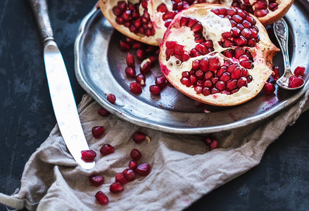 Red ripe peeled pomegranate on rustic metal plate and beige kitchen towel over dark background