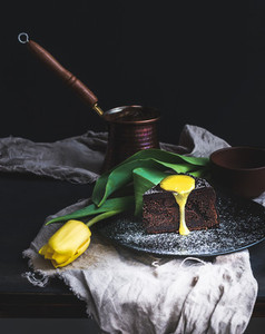 Perfect morning set for woman  Piece of truffle chocolate cake with lemon curd icing  hot coffee and yellow tulip on dark backdrop
