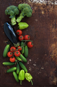 Vegetable mix of garden cherry tomatoes  cucumbers  paprikas  eggplant  broccoli on rusty metal grunge background  top view