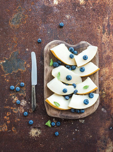 Melon and blueberries in a rustic wooden serving dish over grunge metal rusty background  top view