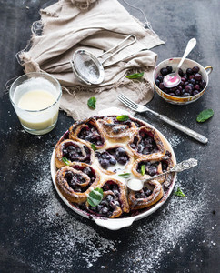 Blueberry buns with fresh mint and creamy sauce on dark backdrop