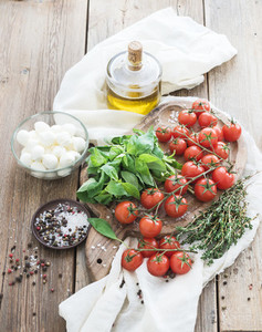 Basil cherry tomatoes mozarella olive oil  salt spices on rustic chopping board over old wood background