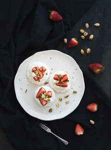 Small strawberry and pistachio pavlova meringue cakes with mascarpone cream fresh mint over black backdrop