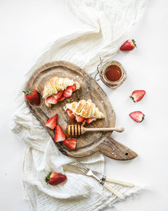 Freshly baked croissants with strawberries  mascarpone and honey on rustic wooden board over white backdrop