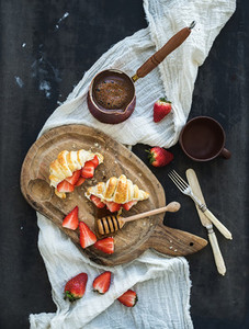 Breakfast set  Freshly baked croissants with strawberries  mascarpone  honey and coffee on rustic wooden board over dark grunge backdrop